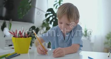 一个穿着蓝色T恤的男孩坐在餐桌旁的<strong>厨房</strong>里，画一支铅笔在做<strong>幼儿</strong>园的作业